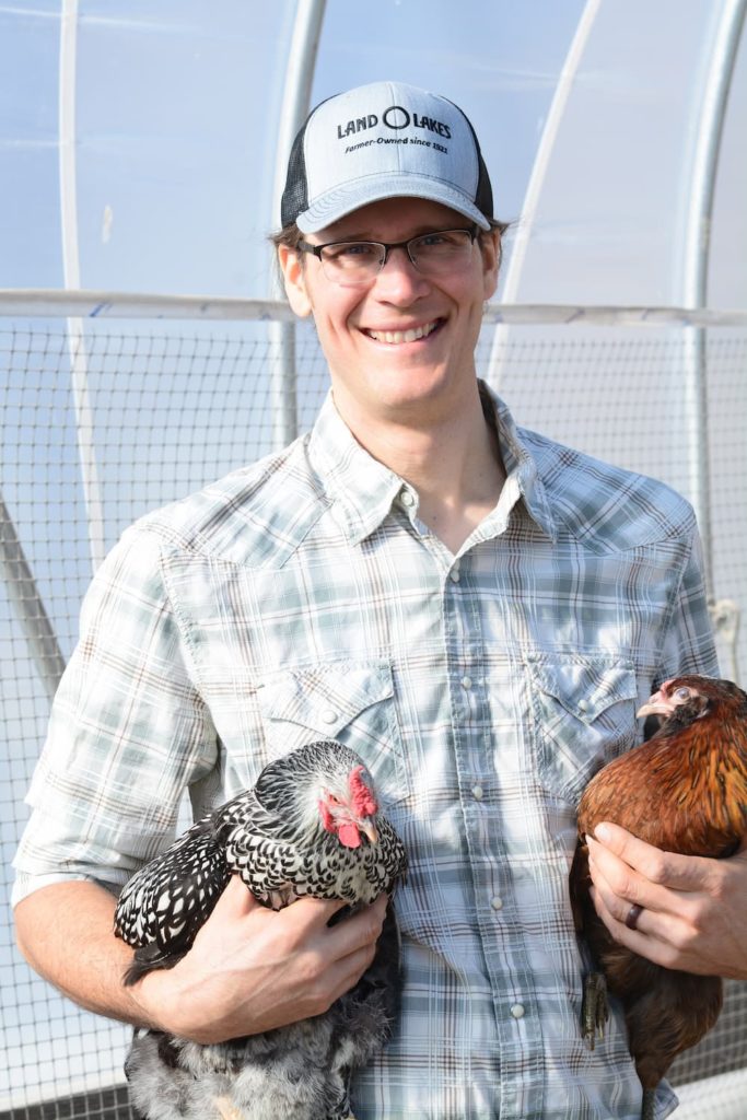 Farmer Matthew holding a chicken under each arm.